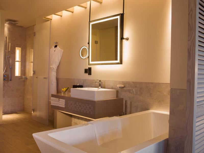Modern bathroom with freestanding bathtub, sink, and illuminated mirror in warm lighting.