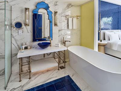 Modernes Badezimmer mit freistehender Badewanne, blauem Teppich, Marmorwänden und blauem Waschbecken.