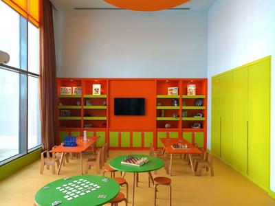 Moderner Klassenraum mit runden Tischen, bunten Stühlen, Bücherregal und großen Fenstern.