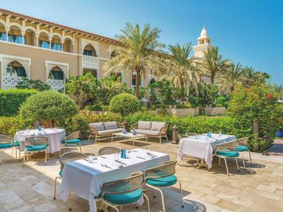 Buitengebied van een hotel met gedekte tafels en palmbomen op een zonnige dag.