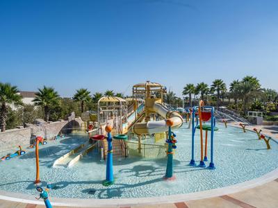 Kinderwasserspielplatz mit Rutschen, Wasserfontänen und Palmen unter klarem blauem Himmel.