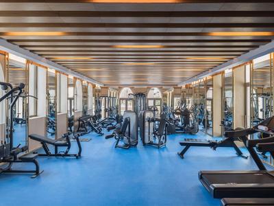 Großer, heller Fitnessraum mit blauen Boden, modernen Geräten und Holzdecke mit Beleuchtung.