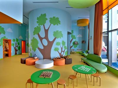 Colorful children's playroom with tree mural, small tables, and seating areas.