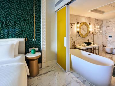 Modernes Hotelzimmer mit weißem Bett, freistehender Badewanne und grün gemusterter Wand.