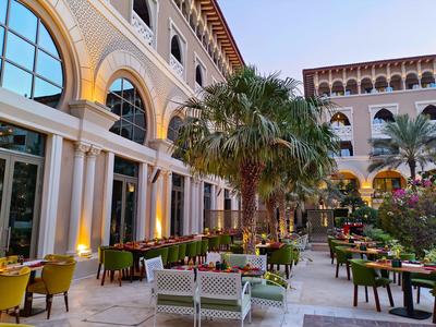 Hotel courtyard with palm trees and colorful chairs in front of large arched windows.