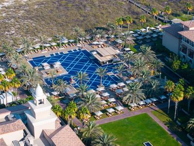 Luxurious resort with a large pool, sun loungers, and surrounded by palm trees.