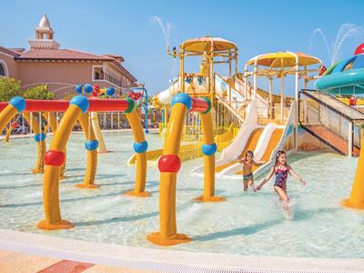 Kinder spielen im flachen Pool mit gelben Wasserspielen und Rutschen bei sonnigem Wetter.