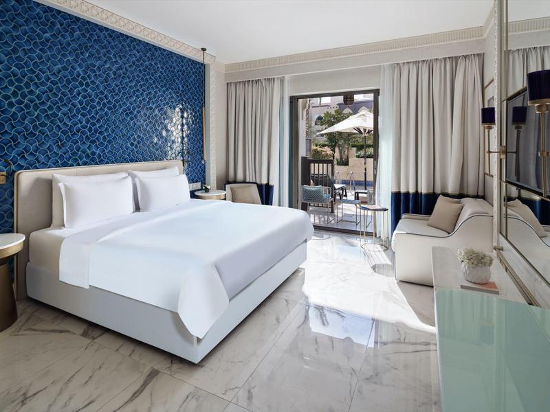 Modern hotel room with king bed, blue accent wall, marble floor, and balcony view.