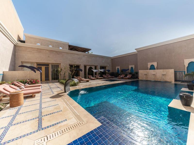 Outdoor pool with seating and towels in a modern, sunlit courtyard at a hotel.