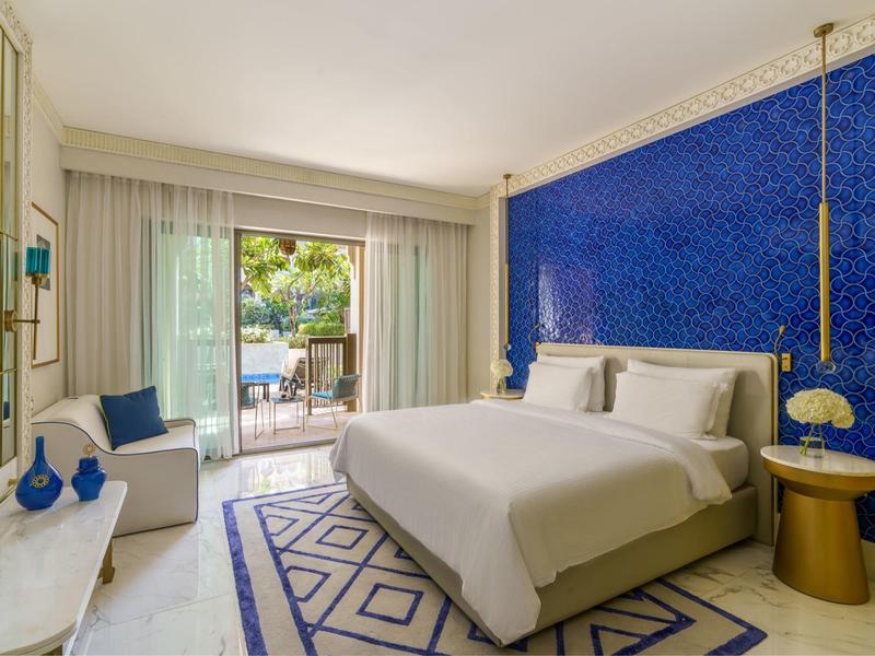 Modern hotel room with king bed, blue accent wall, balcony, and elegant decor.