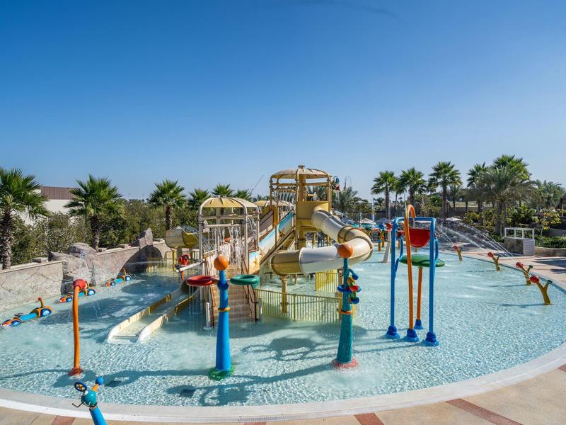 Outdoor water play area with slides and splash features under clear blue sky at a resort.