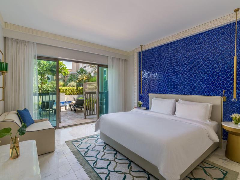 Modern hotel room with king bed, blue accent wall, balcony, and garden view.