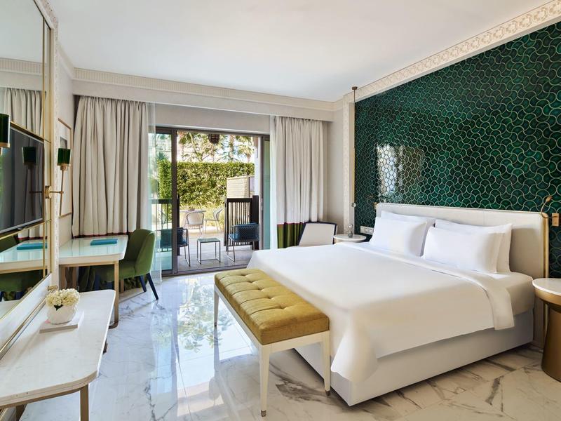 Modern hotel room with large bed, green accent wall, and balcony view of garden.