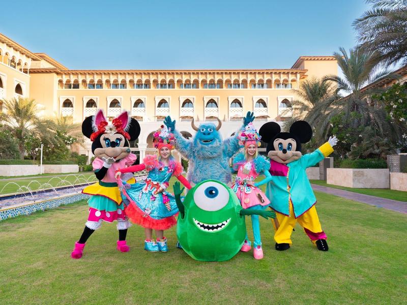 People in colorful costumes in front of a hotel with lawn and blue sky.