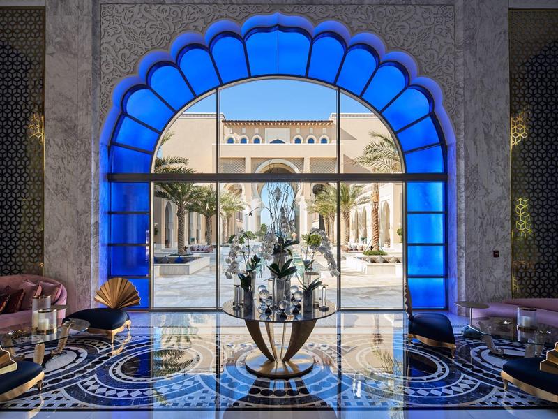 View through a blue-lit arched window onto a garden with palm trees and a statue.