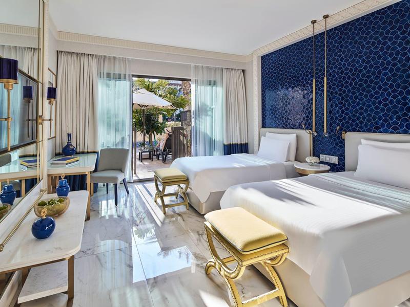 Modern hotel room with two beds, blue accent wall, elegant decor, and access to a terrace.