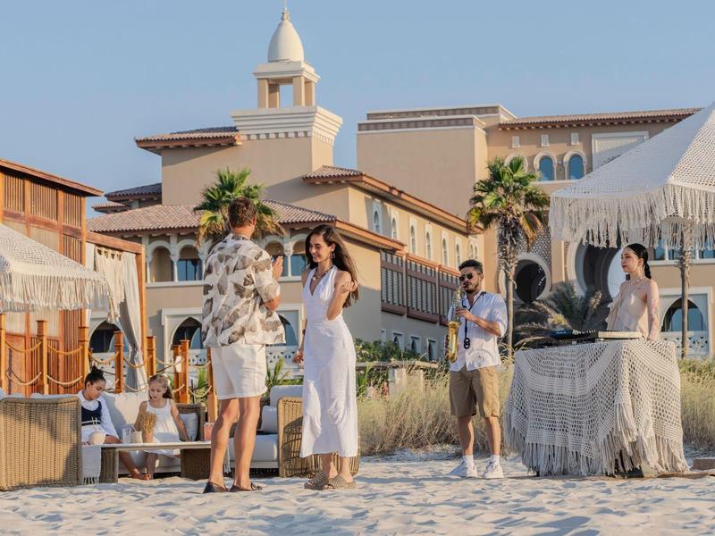 Three people stand on the beach in front of a resort with palm trees and umbrellas.