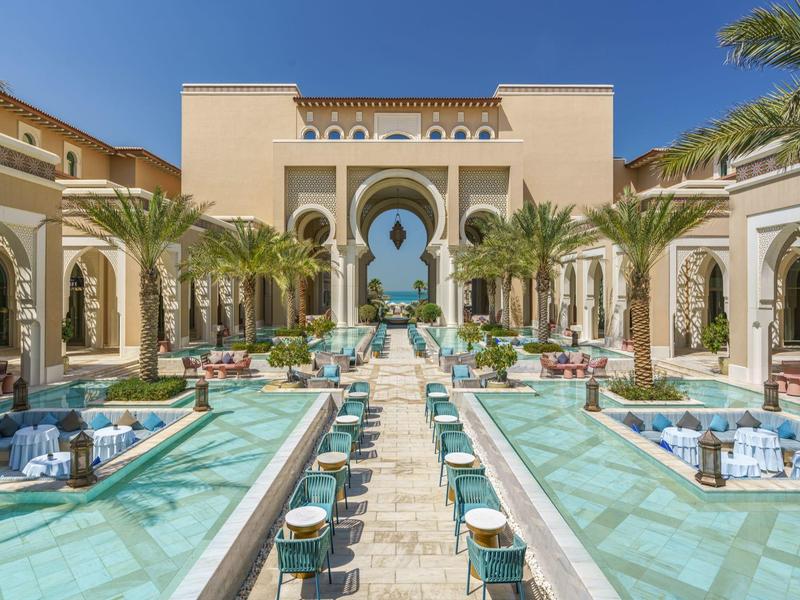 Luxury hotel with pool and elegant Arabian-style architecture under clear sky.