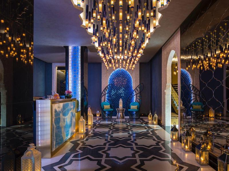 Luxurious hotel lobby with ornate chandelier, patterned floor, and blue artistic wall decor.