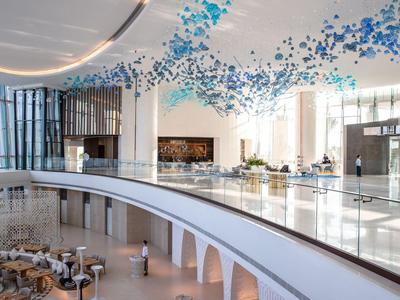 Velká světlá hotelová lobby s moderním designem a modrými dekoracemi na stropě.