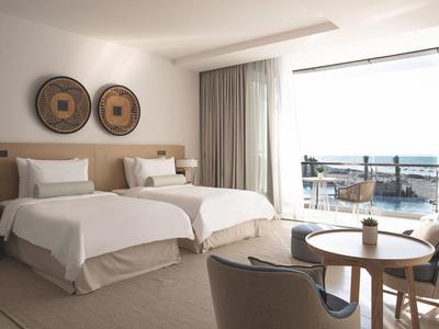 Chambre d'hôtel moderne avec deux lits simples et vue sur la mer à travers de grandes fenêtres.