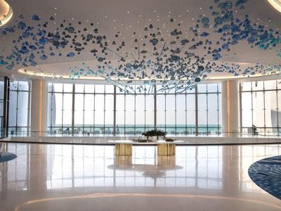 Großer, heller Hotellobby mit großen Fenstern und moderner Deckeninstallation aus blauen Elementen.