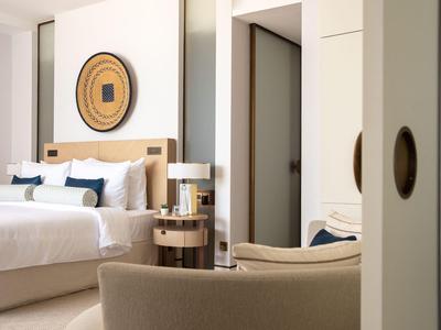 Chambre d'hôtel confortable avec grand lit, table de nuit et fauteuil au design moderne.