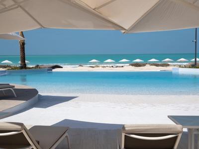 Pohled na infinity bazén s lehátky a bílými slunečníky u moře.