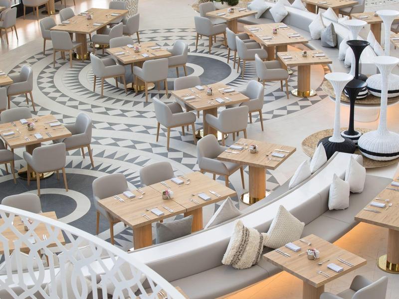 Espace restaurant moderne avec mobilier en bois et blanc et tapis rond décoratif.