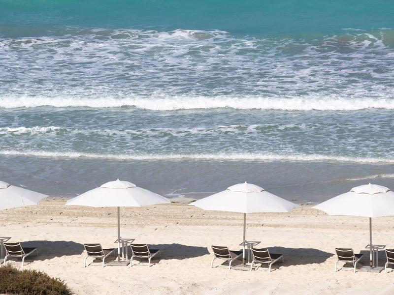 Quatre parasols blancs avec des chaises longues sur une plage de sable au bord de la mer