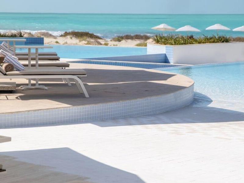 Chaises longues modernes au bord d'une piscine avec vue sur la mer et parasols blancs.