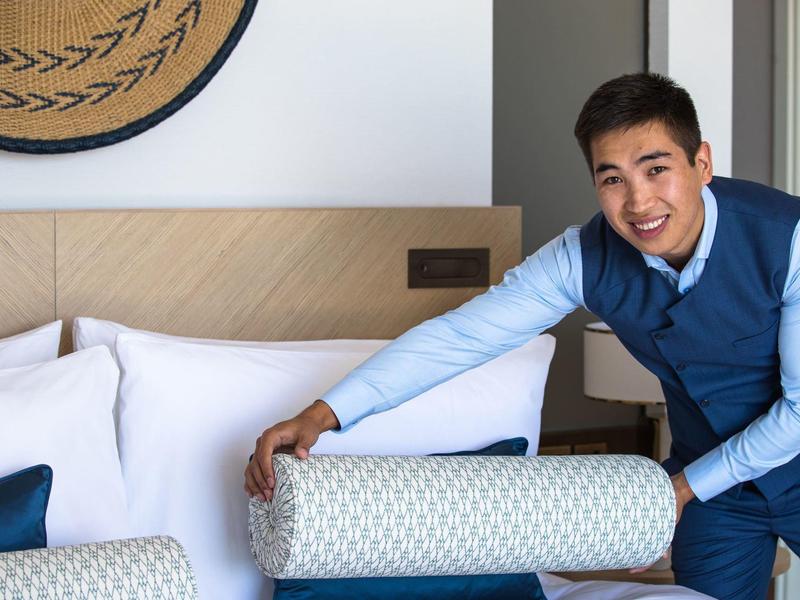 Le personnel de l'hôtel en uniforme arrange un lit avec un coussin décoratif.