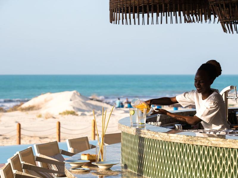 Homme servant des boissons dans un bar de plage avec vue sur la mer et les dunes de sable.