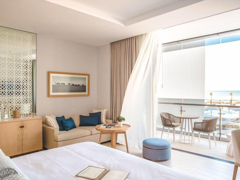 Chambre d'hôtel lumineuse avec balcon, coin salon confortable et vue sur la mer.