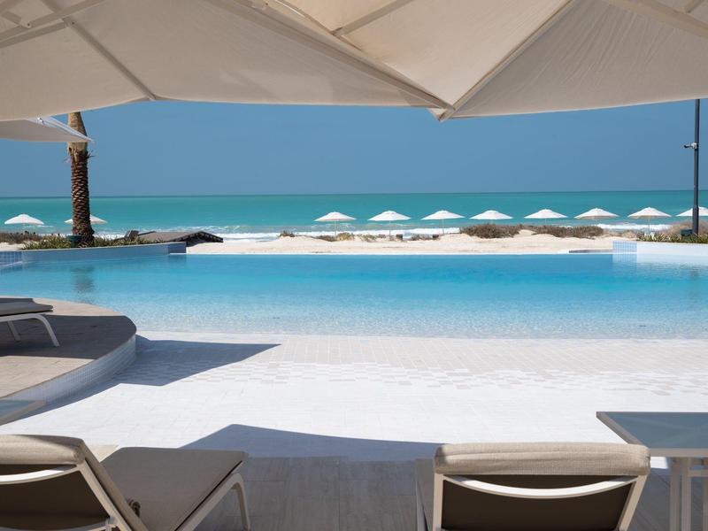Piscine extérieure moderne avec chaises longues et vue dégagée sur la mer par temps clair.