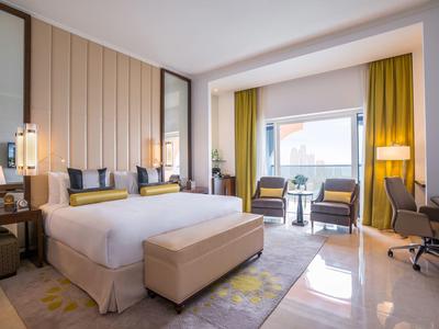 Chambre d'hôtel lumineuse avec grand lit, coin salon et bureau devant fenêtre avec vue.