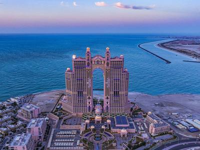 Complexe hôtelier de luxe avec deux tours au bord de la mer, plage étendue et ville environnante.