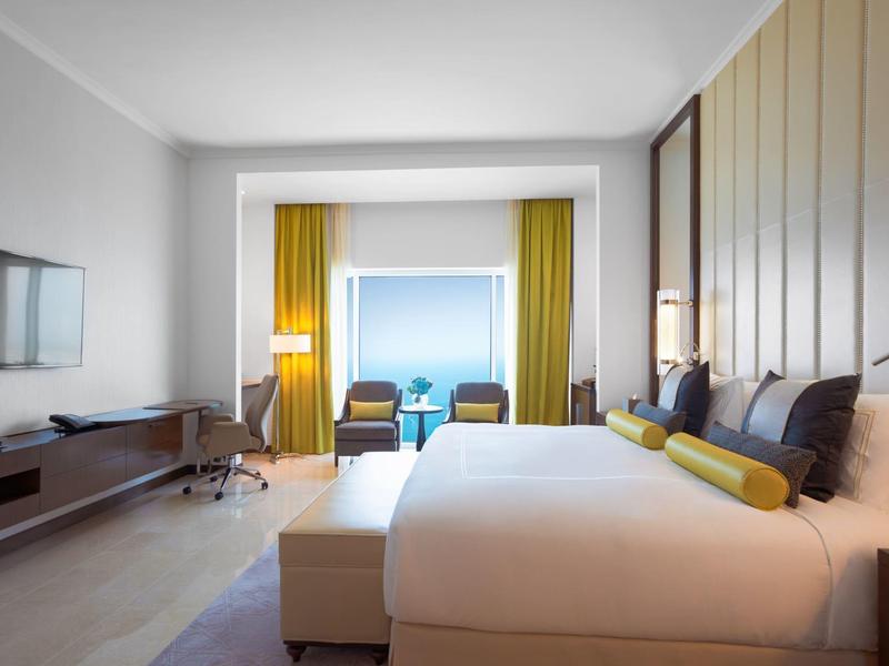 Chambre d'hôtel lumineuse avec grand lit, télévision et coin salon près de la fenêtre.