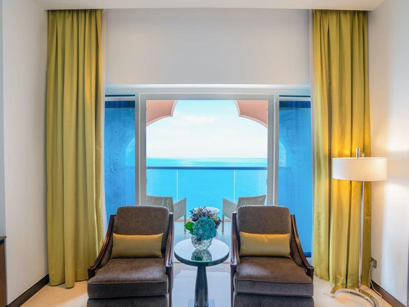 Deux fauteuils avec coussins devant de grandes fenêtres et des rideaux jaunes, vue sur la mer.