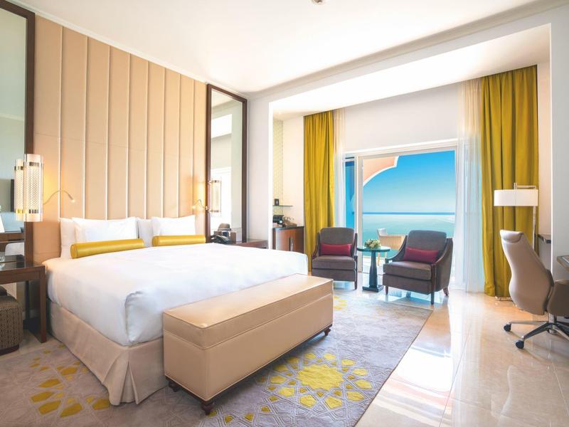 Chambre d'hôtel lumineuse avec grand lit, coin salon et vue sur la mer.