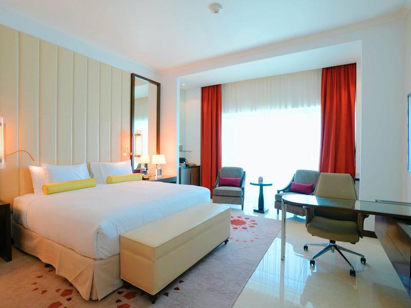 Chambre d'hôtel lumineuse avec grand lit, bureau et rideaux rouges.