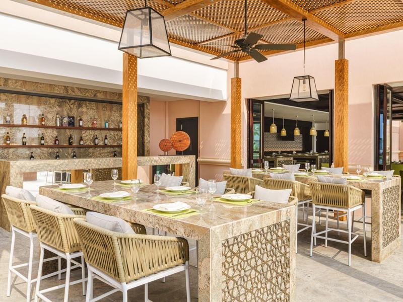 Espace extérieur moderne d'un restaurant avec une grande table en U et des chaises sous une pergola en bois.