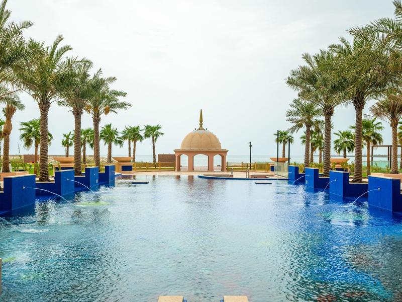 Une grande piscine bordée de palmiers avec un dôme au bout offrant une vue sur la mer.