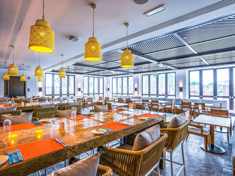 Restaurant moderne et lumineux avec tables en bois, chaises en osier et suspensions jaunes.
