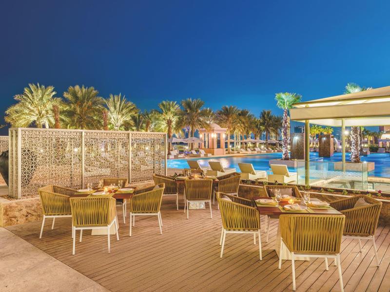 Vue nocturne d'un hôtel avec piscine, palmiers et espace assis en plein air.