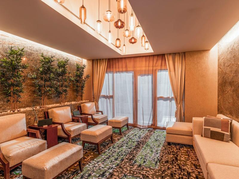 Salle d'attente confortable d'hôtel avec fauteuils, plantes et tapis moelleux.