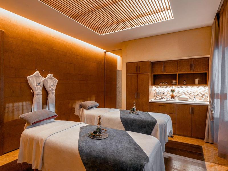 Salle de bien-être confortable avec deux tables de massage, éclairage chaud et accents en bois.