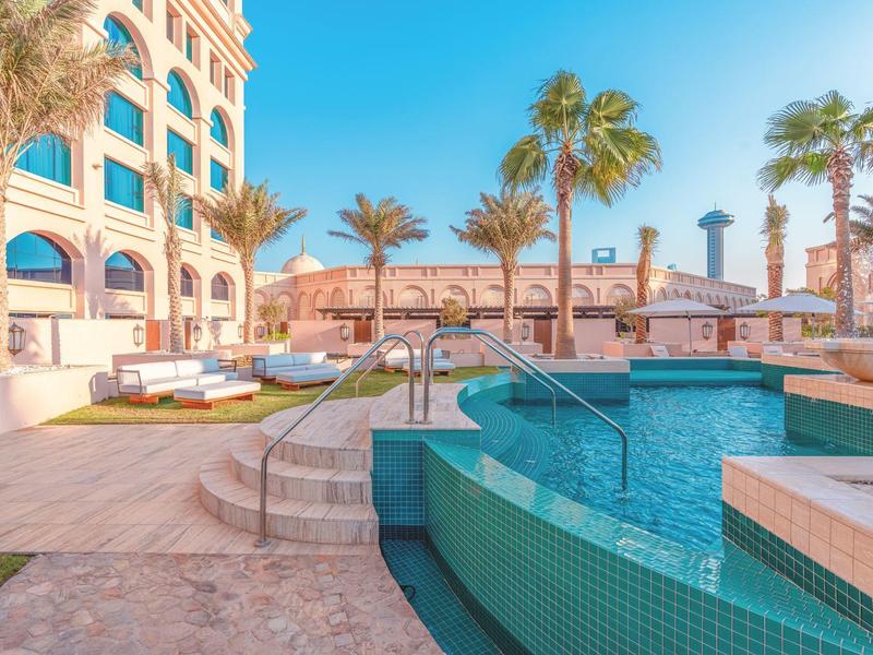 Piscine de luxe d'hôtel avec des palmiers et des espaces de détente sous un ciel bleu.