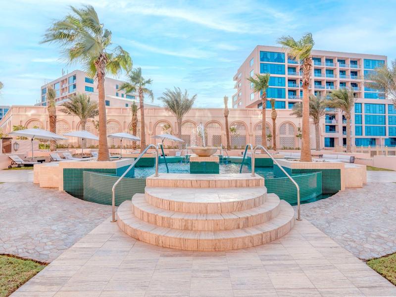 Espace piscine moderne avec escalier et palmiers devant un hôtel