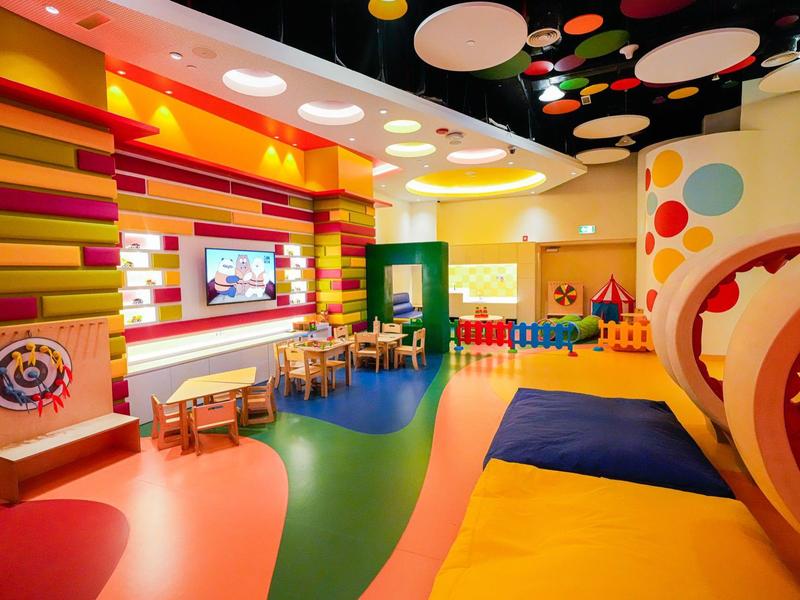 Espace de jeux coloré et moderne pour enfants avec tables de jeux et sièges dans un hôtel.